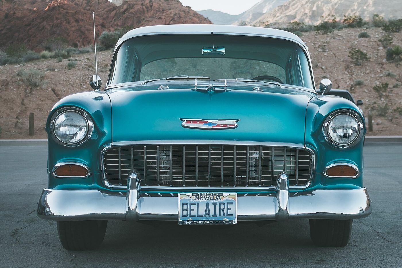 Turkos Chevrolet Bel Air från 1955 rakt framifrån på en tom parkering i ökenlandskap